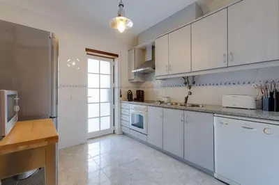 a kitchen with white cabinets and a large window at ROJA PÉ - Elegante apartamento T2 com AC perto do Pine Cliffs in Albufeira