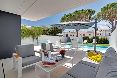 a patio with chairs and an umbrella and a pool at One Six Villa in Vilamoura