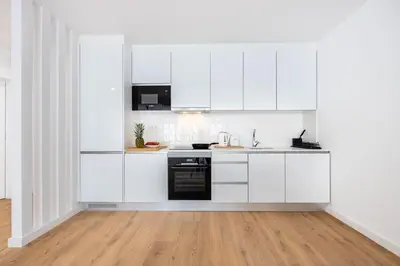 a white kitchen with white cabinets and a wooden floor at Alfamar Inês Apartment in Albufeira