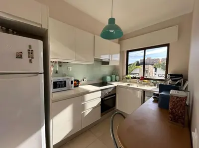 a kitchen with white cabinets and a table in it at Falésia Beach Apartment in Albufeira