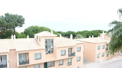 a large pink building with trees in the background at Bicos Beach Apartments By Albufeira Rental in Albufeira
