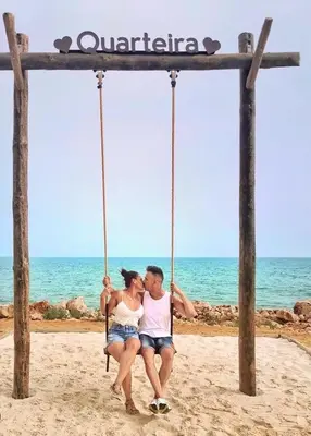 a man and woman sitting on a swing on the beach at Studio Praia de Quarteira in Quarteira