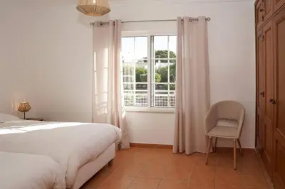 a bedroom with a bed and a chair and a window at Jardins da Galé Beach House in Albufeira