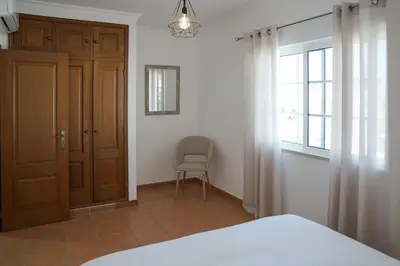 a bedroom with a bed and a window and a chair at Jardins da Galé Beach House in Albufeira