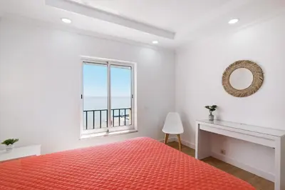 a white bedroom with a red bed and a window at Moderno e renovado T2 in Quarteira