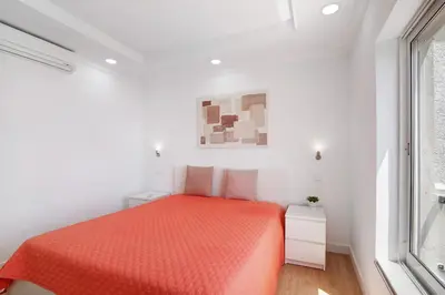 a white bedroom with a orange bed and a window at Moderno e renovado T2 in Quarteira