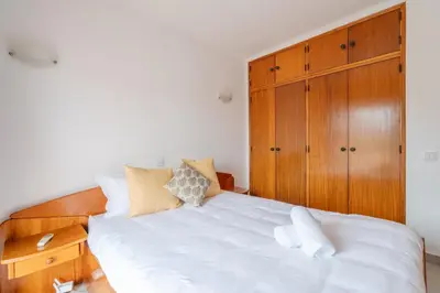 a bedroom with a white bed and a wooden cabinet at Sunshine Holiday House in Quarteira