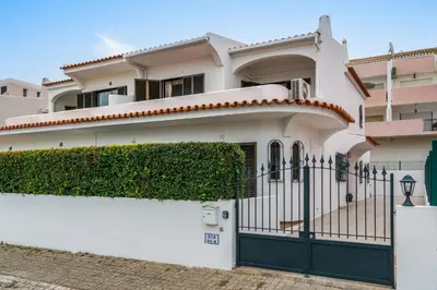 a white house with a gate and hedge at Sunshine Holiday House in Quarteira
