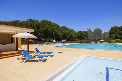 a pool with chairs and a table and an umbrella at Central Algarve Duplex Retreat with Garden & Pool in Quarteira
