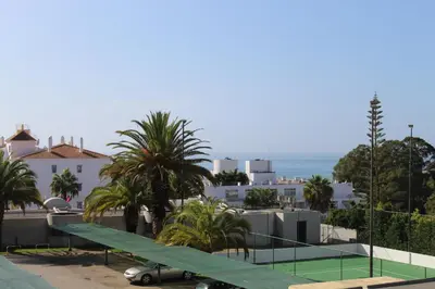a tennis court with palm trees and the ocean at Casa Oura Sea Living in Albufeira