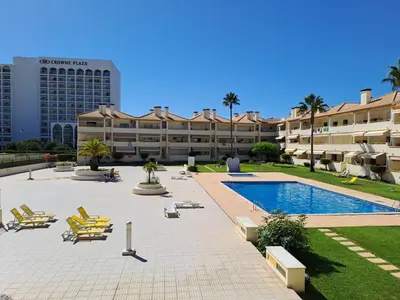 a resort with a pool and chairs and a building at T2 Vila Atlântida Praia Vilamoura in Quarteira