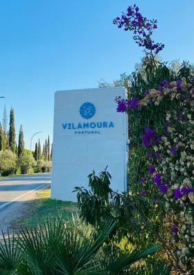 a sign in front of a road with purple flowers at Solar Dos Pinheiros in Quarteira
