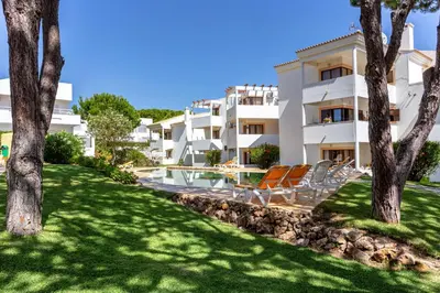 a building with chairs and trees in front of it at Host Wise - Fresh Sunny Flat with Pool & Terrace in Olhos de Água