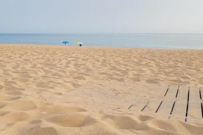 a sandy beach with an umbrella and a bench on it at Sunny Days beach apartment in Quarteira