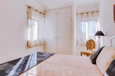 a white bedroom with a bed and a chair at Apartamento Estrela do Mar in Quarteira