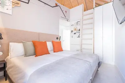a bedroom with a large white bed with orange pillows at LODO Suites Ala - Studio mezanino by HD in Faro