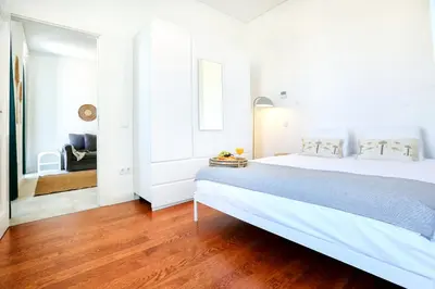 a white bedroom with a large white bed and wooden floors at Lovely Faro Apartment in Faro