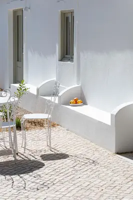 a white building with chairs and a table and a bowl of oranges at Âmago Guesthouse in Santa Bárbara de Nexe