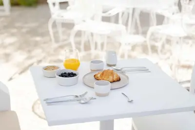 a white table with a plate of food and orange juice at Âmago Guesthouse in Santa Bárbara de Nexe