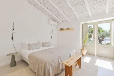a white bedroom with a large bed and a window at Âmago Guesthouse in Santa Bárbara de Nexe