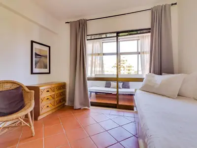 a bedroom with a bed and a chair and a window at AL - Apartamento Moural in Quarteira