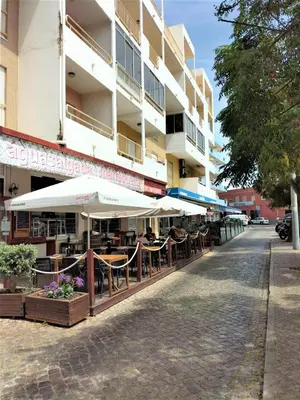 an outdoor cafe with tables and umbrellas in front of a building at T2 Requinte e Vista Mar 4 pax in Quarteira