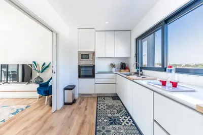 a kitchen with white cabinets and a large window at Stunning 3 BDR Flat W/ Rooftop Pool by LovelyStay in Albufeira