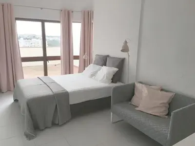 a bedroom with a bed and a chair and a window at CASA Vila Magna T0 in Albufeira