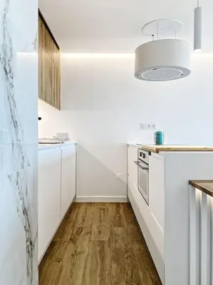 a kitchen with white cabinets and a wooden floor at Front Sea Apartment Quarteira in Quarteira