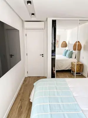 a white bedroom with a bed and a mirror at Front Sea Apartment Quarteira in Quarteira