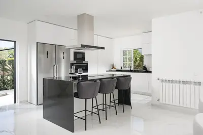 a white kitchen with a black island with bar stools at Villa Olivia in Almancil