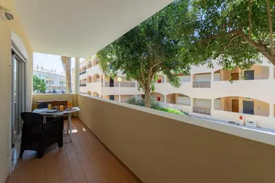 a balcony with a table and trees in a building at Centralgarve - Spacious & Elegant - Vilamoura w Pool - Jacarandás in Quarteira