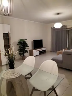 a living room with a glass table and white chairs at T2 Infante Moderno Wi-Fi Garagem 50 M Praia in Quarteira