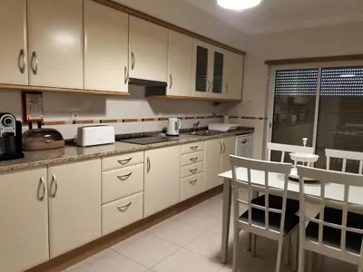 a kitchen with white cabinets and a table and a chair at T2 Infante Moderno Wi-Fi Garagem 50 M Praia in Quarteira