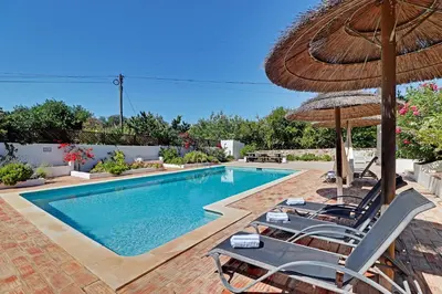 a swimming pool with chairs and an umbrella at Quinta Boliqueime by Portucasa in Boliqueime