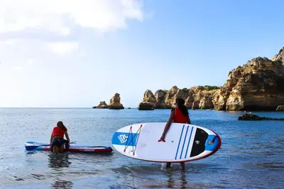 two people standing in the water with surfboards at Espaçoso apt T2, em Olhos Agua in Albufeira