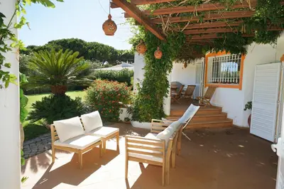 a patio with white chairs and a pergola at Villa Pinheiro Manso in Albufeira