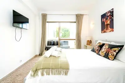 a white bedroom with a large bed and a television at Spacious 1 bed in Vilamoura, Fast Wifi & Pool in Quarteira