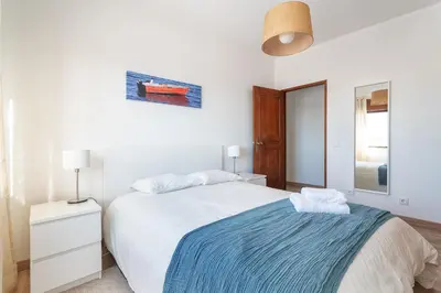 a white bedroom with a bed with a blue blanket at HostWise - Spacious & Sunny Flat - Loulé in Loulé