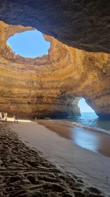 a cave on the beach with people standing on the sand at Domek v srdci Fara in Faro