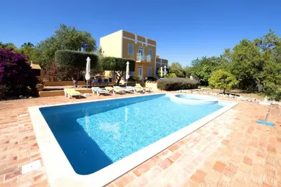 a swimming pool with chairs and a building in the background at Quinta Amarela XL by Portucasa in Loulé