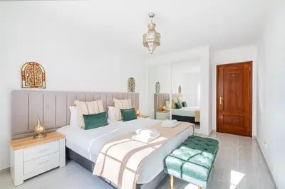 a white bedroom with two beds and a chair at Notre Damme Apartment in Albufeira