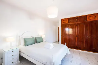 a bedroom with a white bed and a wooden cabinet at Villa Guerreiro in Albufeira