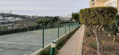 a tennis court with a net and some trees at Encosta Da Orada in Albufeira