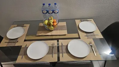 a table with white plates and forks and a bowl of fruit at Newly refurbished 2 bed appt Vilamoura in Vilamoura