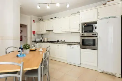 a kitchen with white cabinets and a wooden table at Roberto Quarteira Central in Quarteira