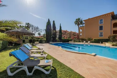 a pool with lounge chairs and an umbrella next to a building at Avenue Apartment Vilamoura in Quarteira