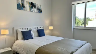 a white bedroom with a large bed with blue pillows at Hibisco 2 by Check-in Portugal in Albufeira