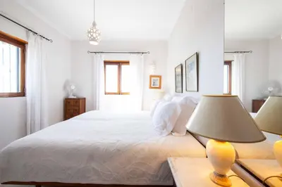 a white bedroom with a bed and a lamp on a table at Villa Jacaranda Bordeira in Corotelo