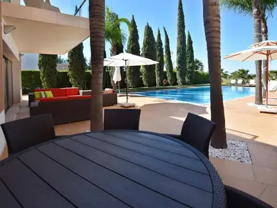 a table and chairs with a pool and palm trees at Special Vilamoura Villa 6 Bedrooms Villa Lagoon Private Pool in Quarteira